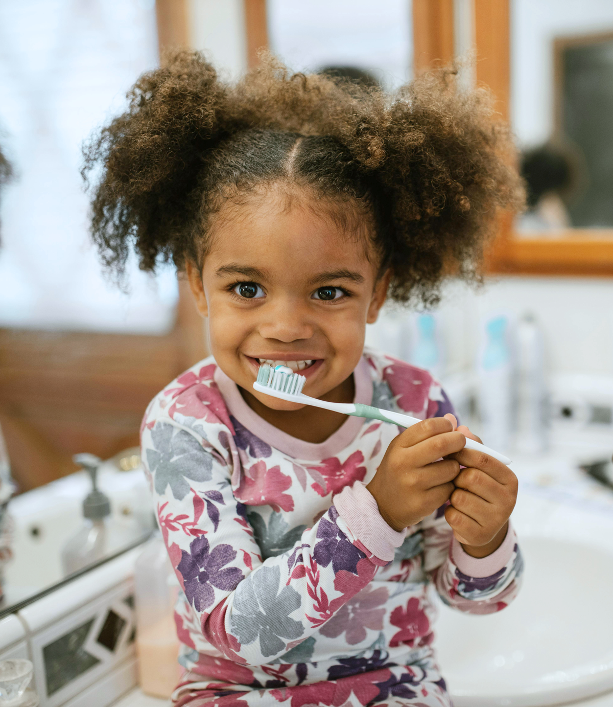 Smiling child holding a toothbrush in bathroom.