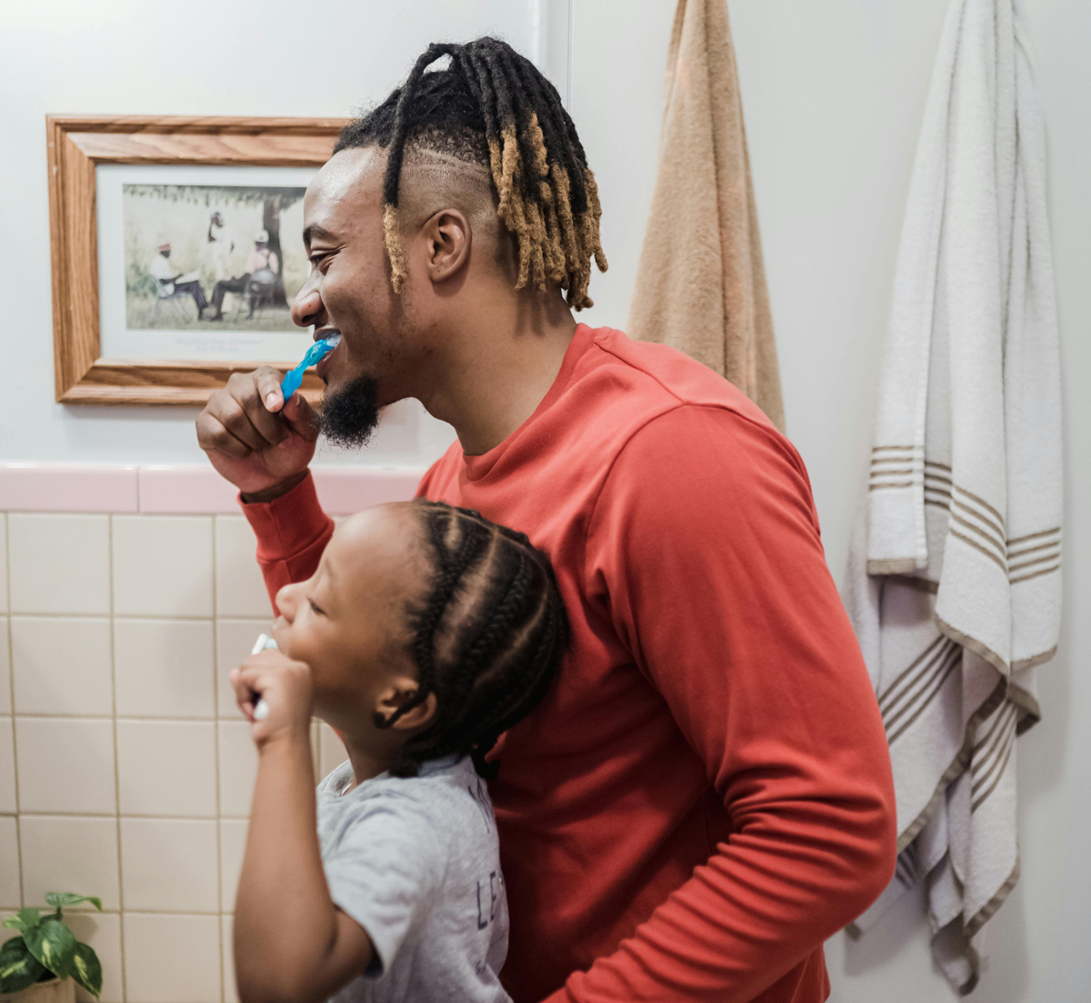 Father and child brushing teeth together, smiling.