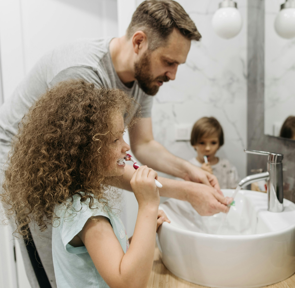 Parent and children brushing teeth together in bathroom.