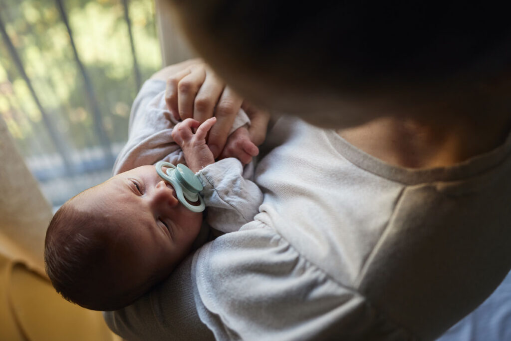 Baby with pacifier cradled in caregivers arms