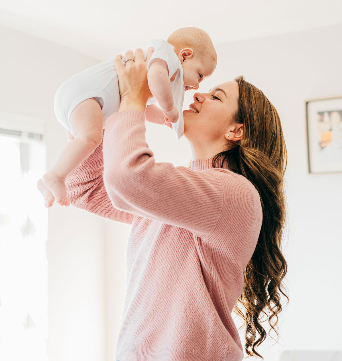 Woman joyfully lifts baby, smiling in sunlit room