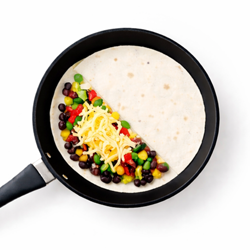 Tortilla filled with colorful vegetables and cheese in skillet.