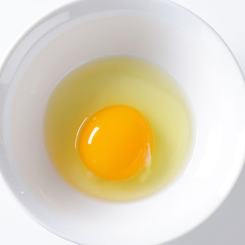 Raw egg in white bowl on plain background.