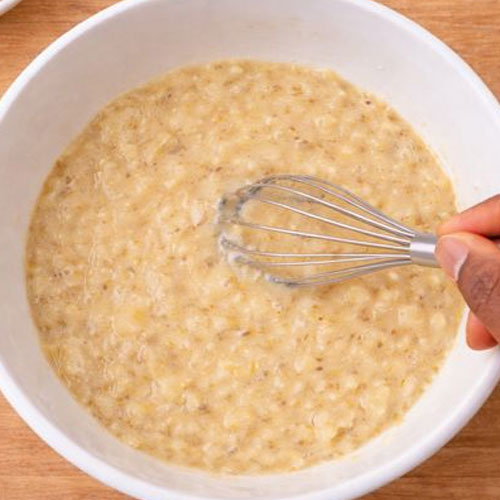 Whisk stirring mashed bananas in white bowl.