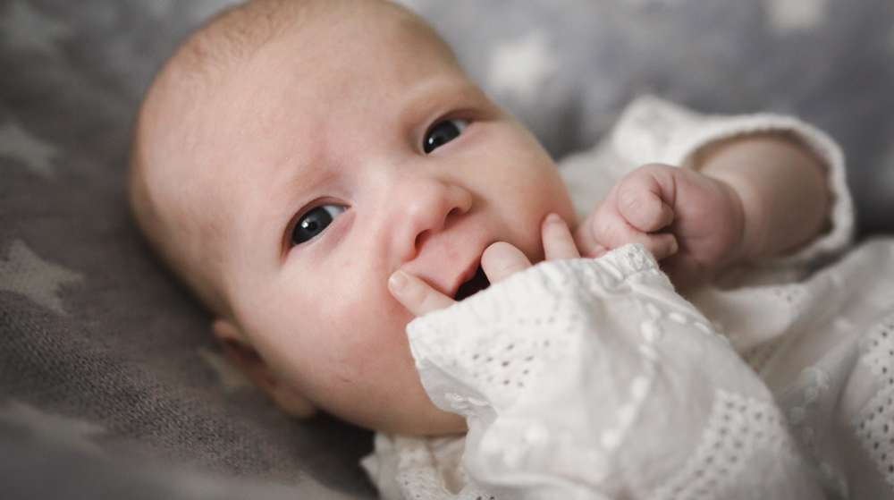 Baby wearing white lace, touching fingers to mouth