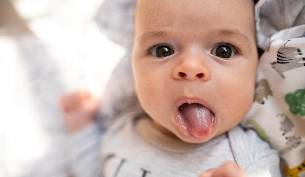 Baby sticking out tongue while lying down