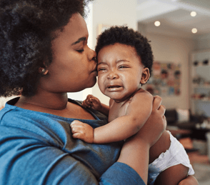 Parent comforting crying baby with a gentle kiss.
