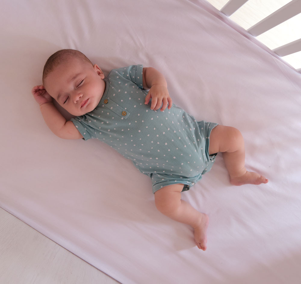 Baby sleeping peacefully in crib wearing polka-dot onesie