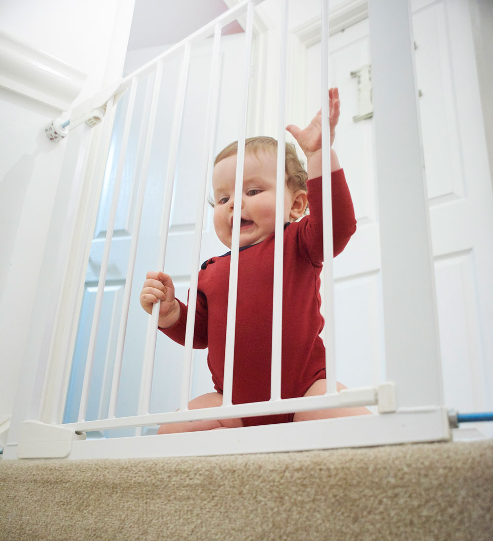 Baby in red onesie behind white safety gate