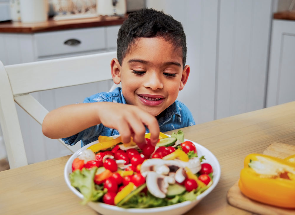 Young boy happily eating fresh vegetable salad
