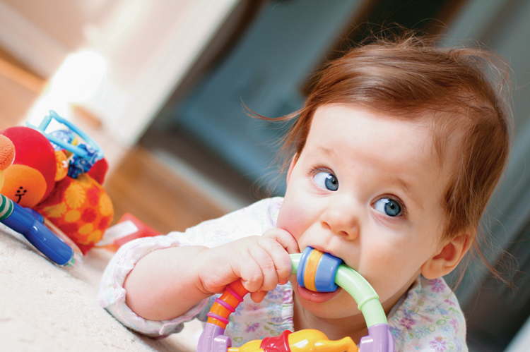 Baby chewing colorful toy on carpet