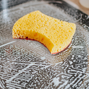 Yellow sponge cleaning soapy glass surface