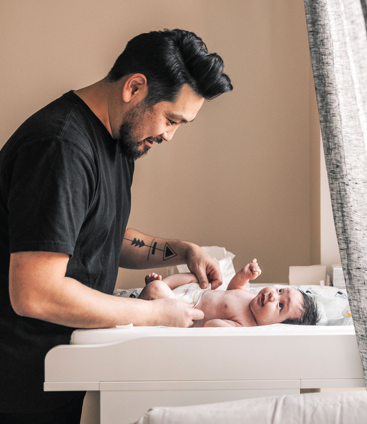 Father changing infants diaper, smiling gently