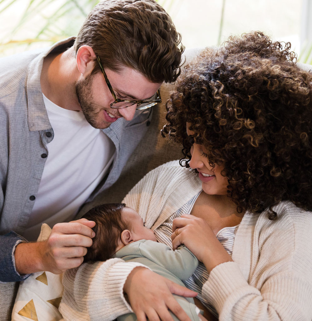 Couple lovingly watching baby breastfeed on couch