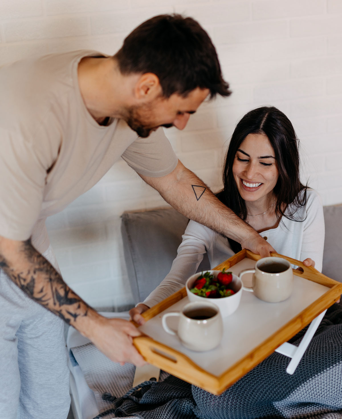Man serves woman breakfast in bed with smiles