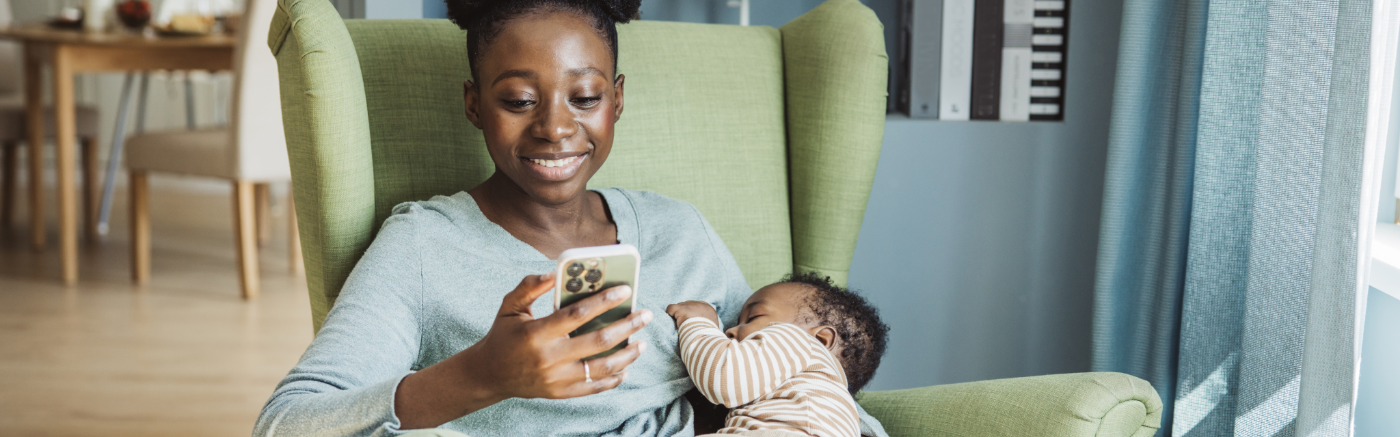 Woman smiling at phone while holding sleeping baby.